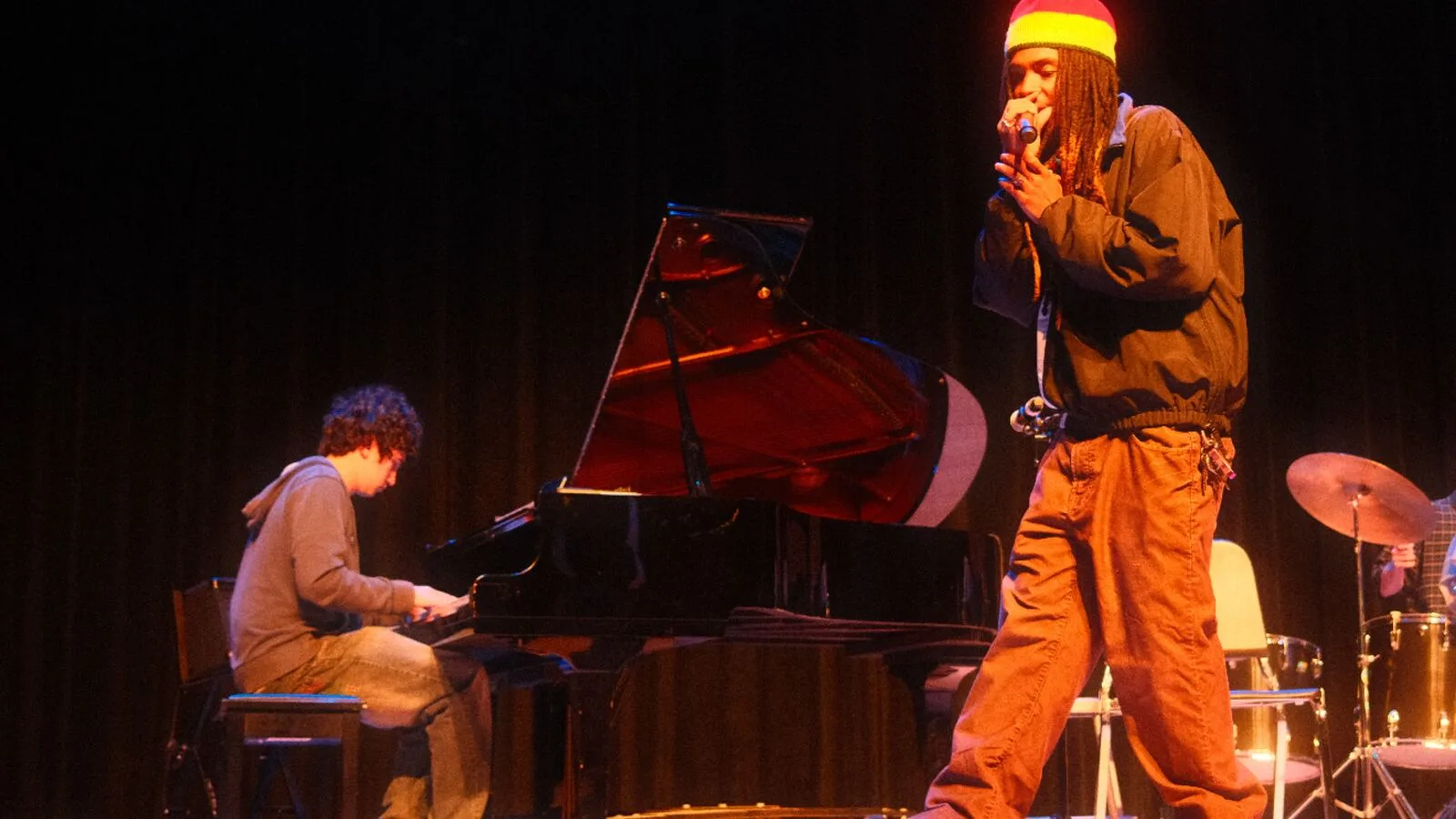 An artist performing on stage beside a grand piano