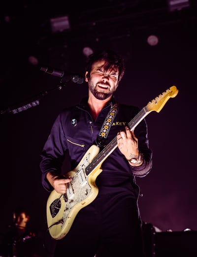 Photograph of singer-songwriter Shakey Graves playing guitar in a low-lit concert venue with purple backlighting.
