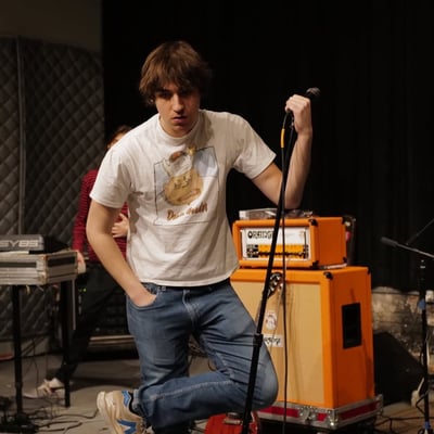 A musician kneeling beside an orange amplifier on stage