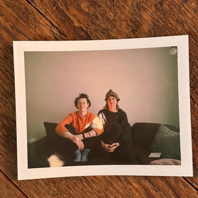 A polaroid lying on a wooden table showing two people on a couch