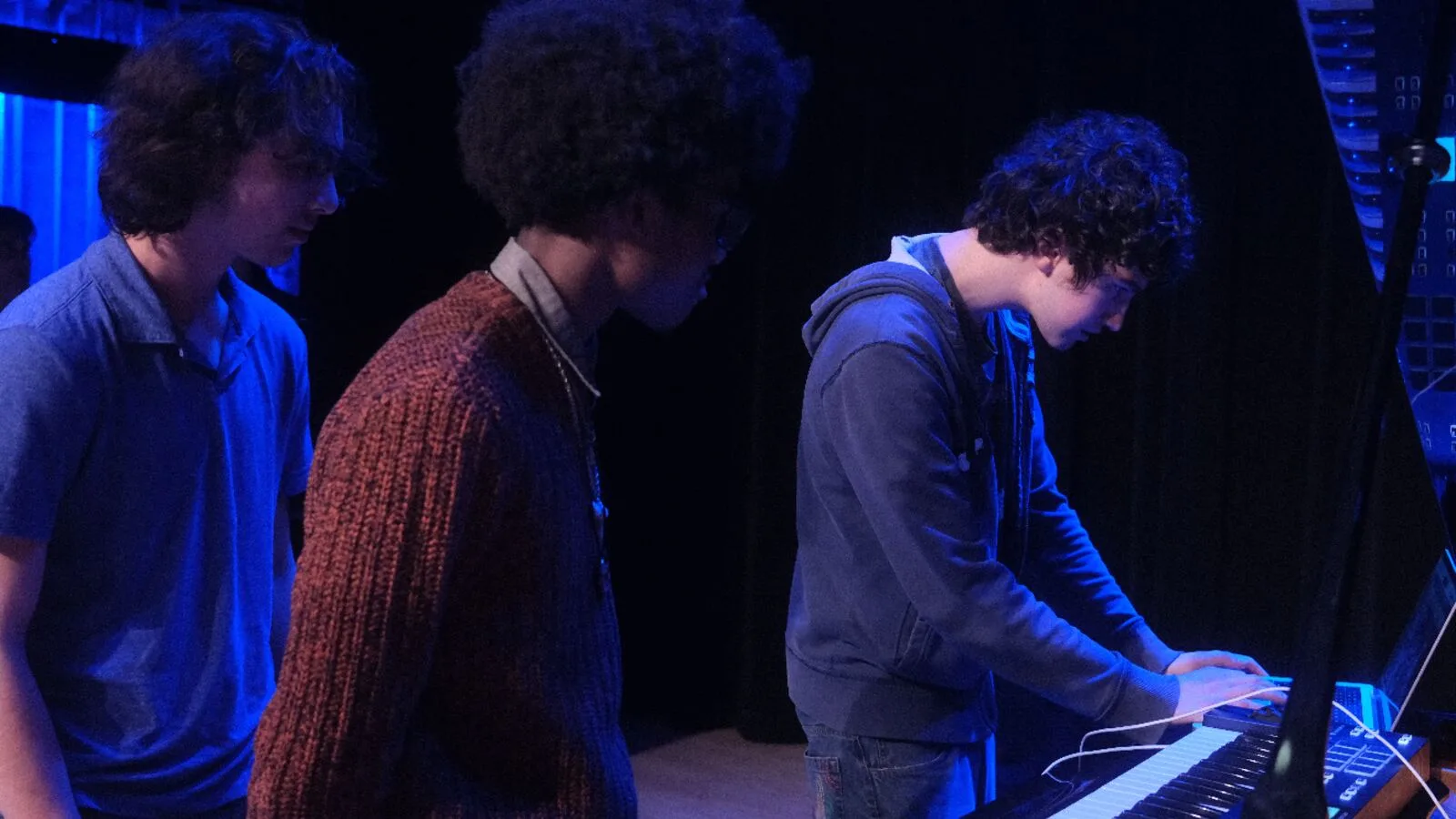 Young musicians playing keyboards under blue light